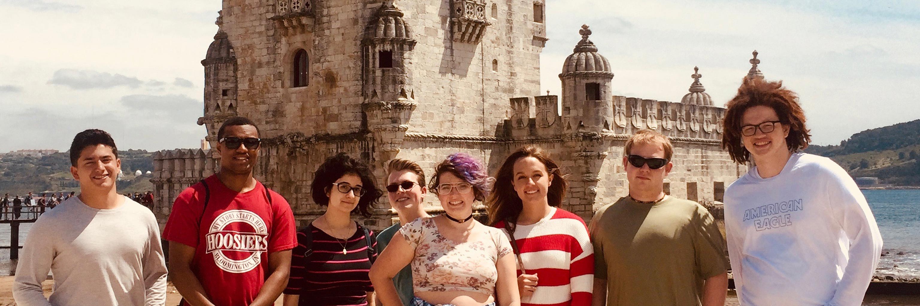 A large group of students smile in front of an ornate building located in their study abroad destination 