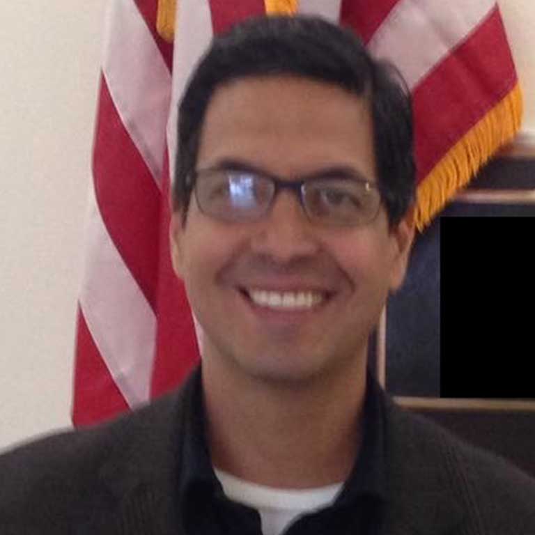 A headshot of Manuel Díaz-Campos, who wears glasses and a dark red dress shirt.