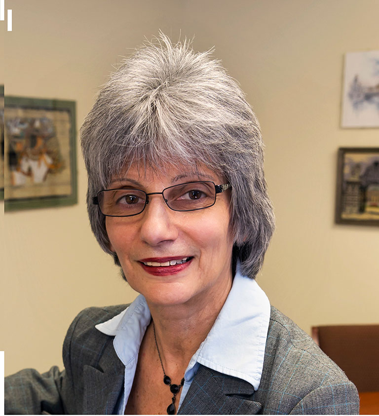 A headshot of Kathleen Sideli, who wears a gray suit and glasses.