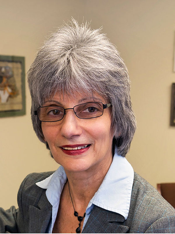 A headshot of Kathleen Sideli, who wears a gray suit and glasses.