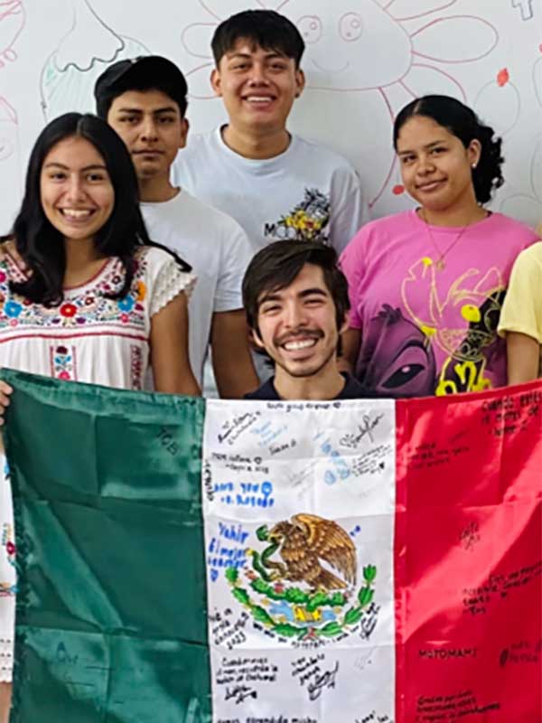 Andres Ayala holds up a signed Mexican flag among a group of people.