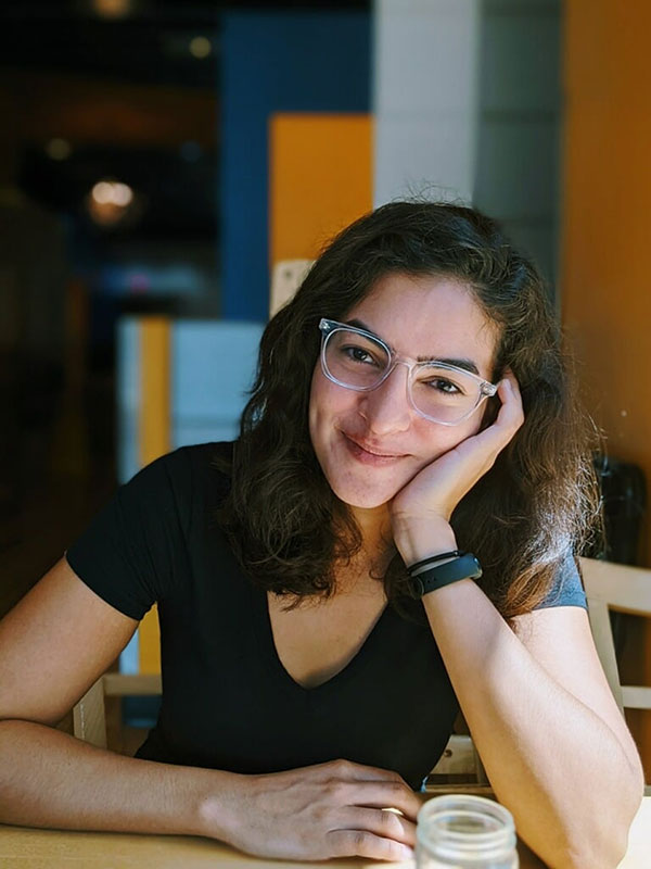 A headshot of Andreina Colina Marin, who poses at a table and wears a black shirt.