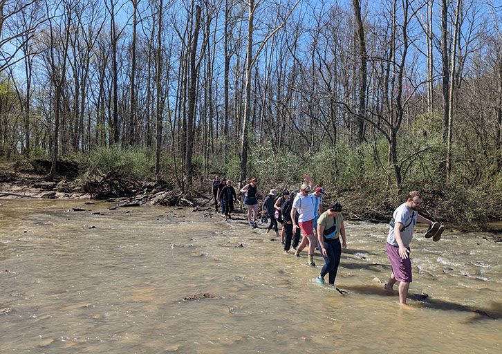 A group of people cross a wide, shallow stream.