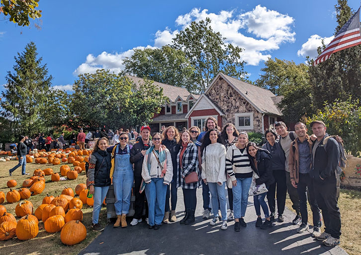 People pose with pumpkins in front of a stone house.