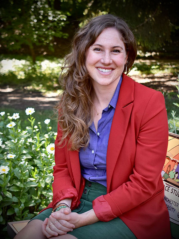 A headshot of Mackenzie Coulter-Kern, who wears a red blazer and poses outside.