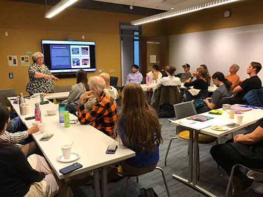 A person standing at the front of a classroom giving a presentation to a seated audience.