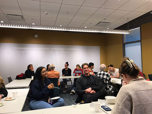 Students and faculty seated around tables talking and eating during a casual gathering.