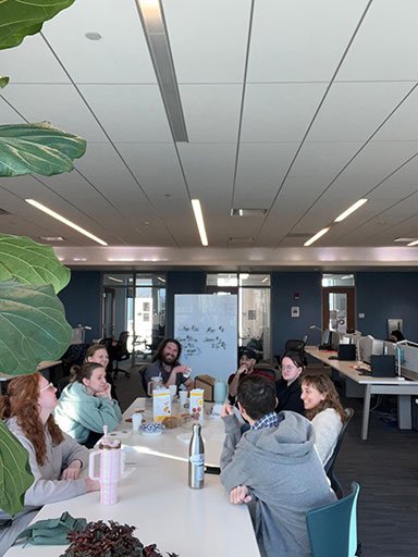 Group of colleagues seated around a long table in a bright office space during an informal discussion.